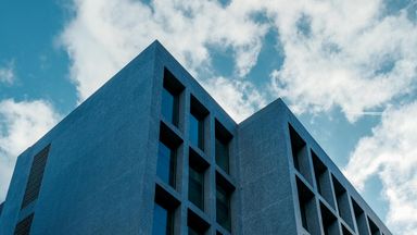 Fachada de um prédio residencial moderno com janelas alinhadas e céu azul ao fundo.